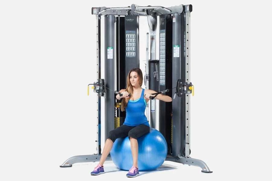 Woman in blue tank top and black capris using TuffStuff Evolution Corner Multi-Functional Trainer with dual cable stations an
