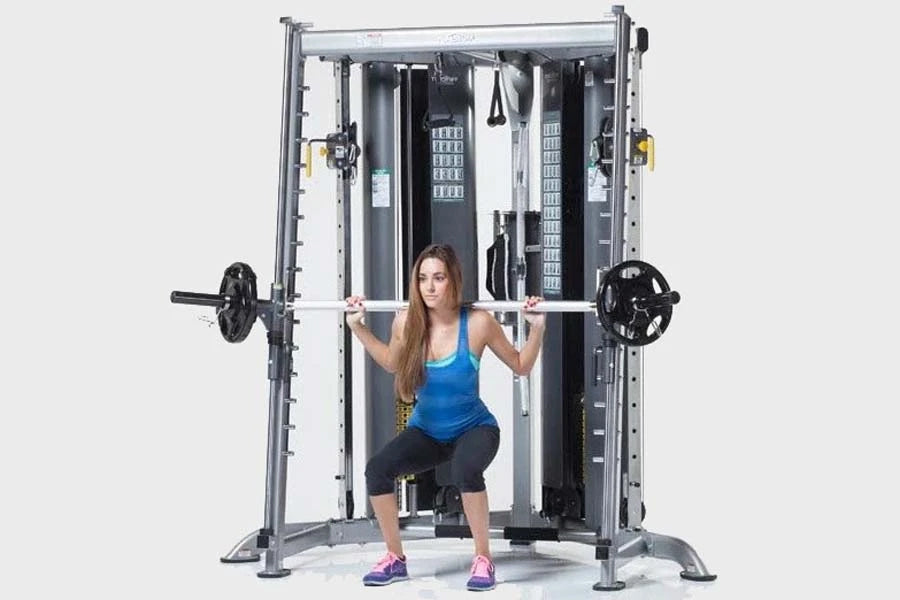 Woman performing squat with barbell on TuffStuff Evolution CXT-225 Smith Press Attachment, wearing blue tank top and black ca
