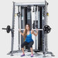 Woman in blue tank top and black capris performing squat exercise on silver and black multi-functional trainer home gym syste