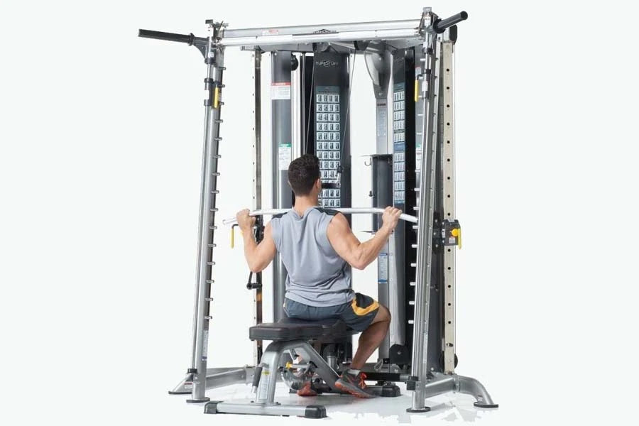 Man using silver and black multi-functional gym trainer with Smith press attachment, seated on bench performing upper body ex