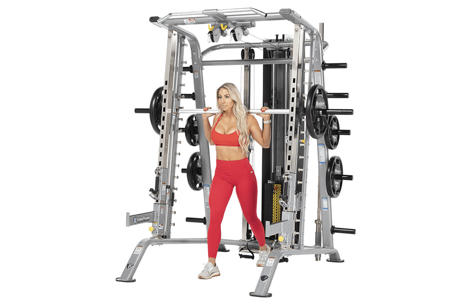 Silver and black Smith machine with weight plates, worn by model in red sports bra and leggings on white background