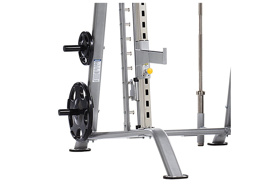 Gray and black Smith machine with dual weight plate pegs, adjustable safety bars, and foot platform on white background