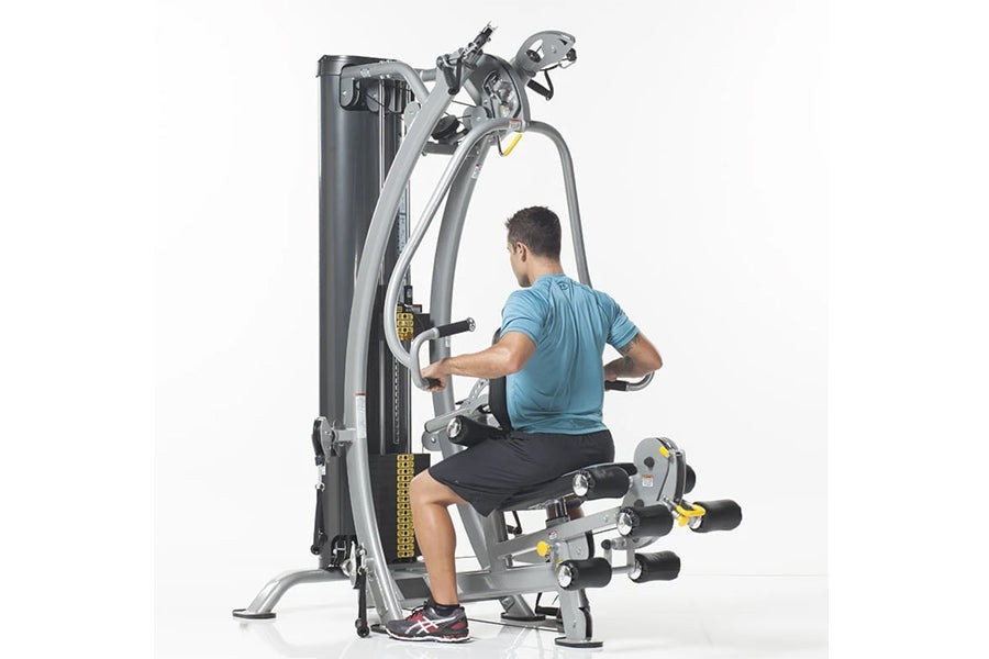 Man in blue shirt using gray and black multi-station home gym machine with cable system on white background