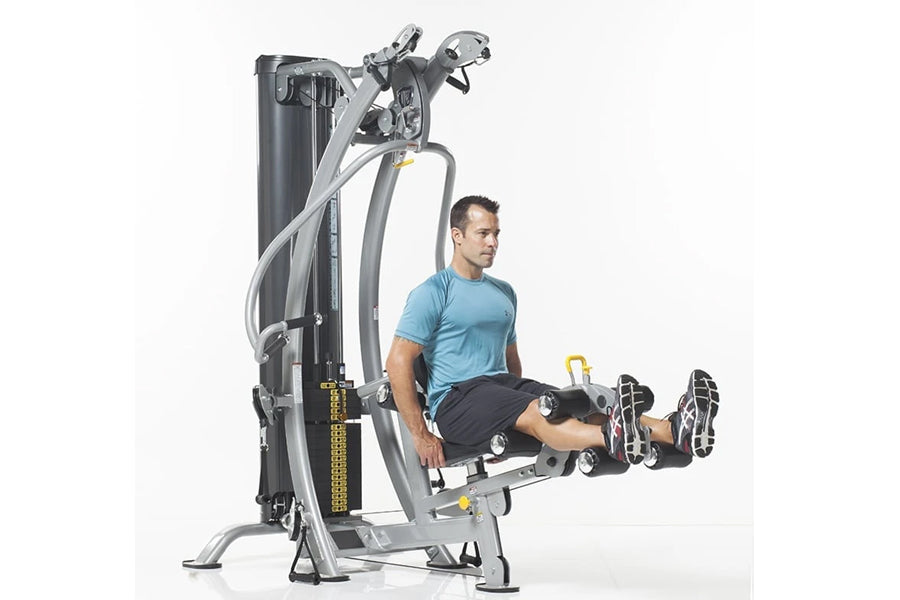 Man in blue shirt using leg press attachment on TuffStuff gray and black hybrid home gym machine against white background