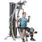 Man in blue shirt using TuffStuff Hybrid Home Gym with dual weight stacks and cable arms on white background
