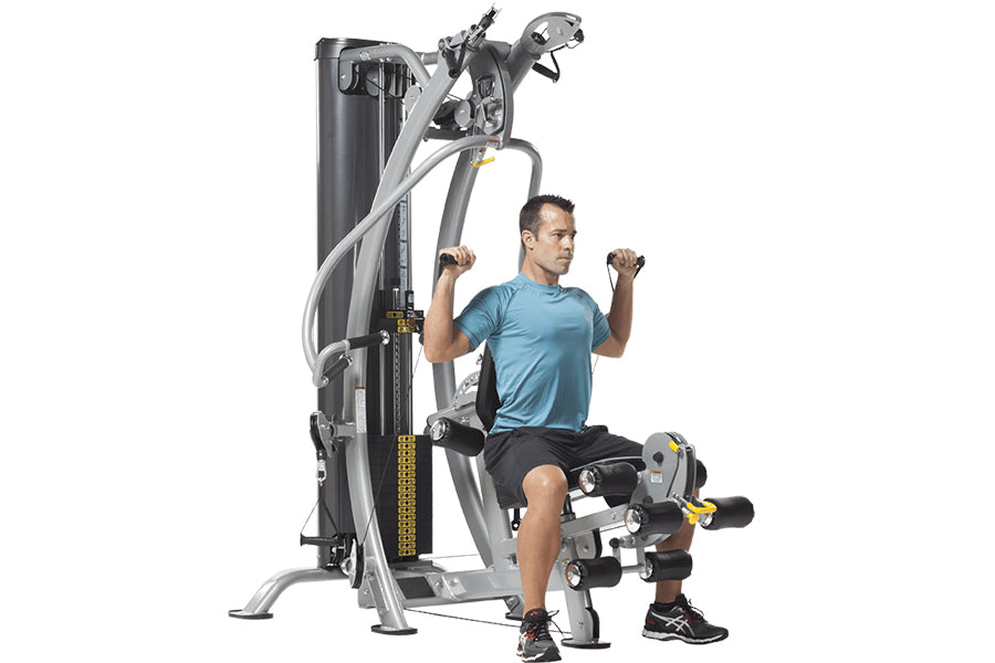 Man in blue shirt using TuffStuff Hybrid Home Gym with dual weight stacks and cable arms on white background