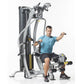 Man in blue shirt using silver and black multi-station home gym machine with adjustable arms and leg press on white backgroun