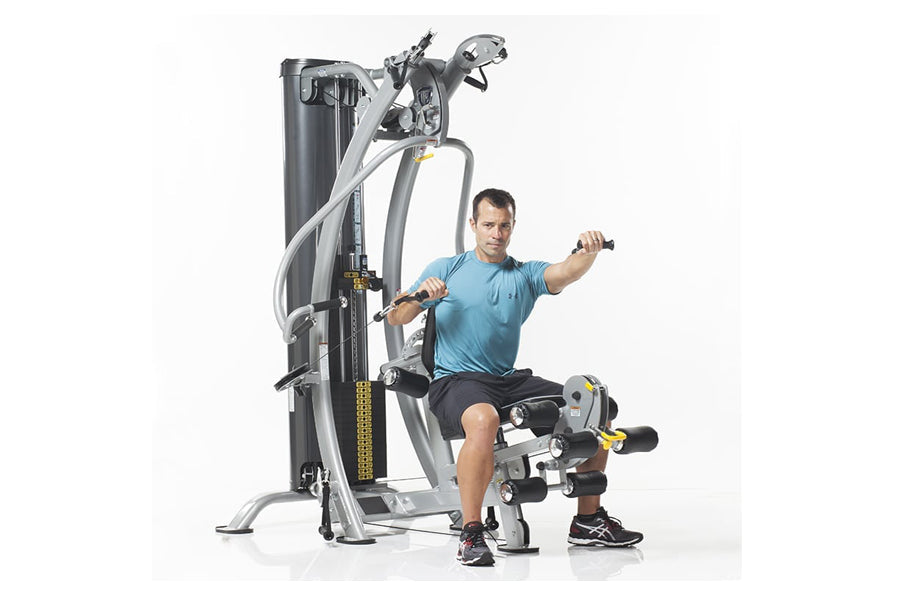 Man wearing blue shirt using silver and black multi-station home gym machine with leg press attachment on white background
