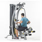 Man in blue shirt using gray and black multi-station home gym machine with leg press attachment on white background