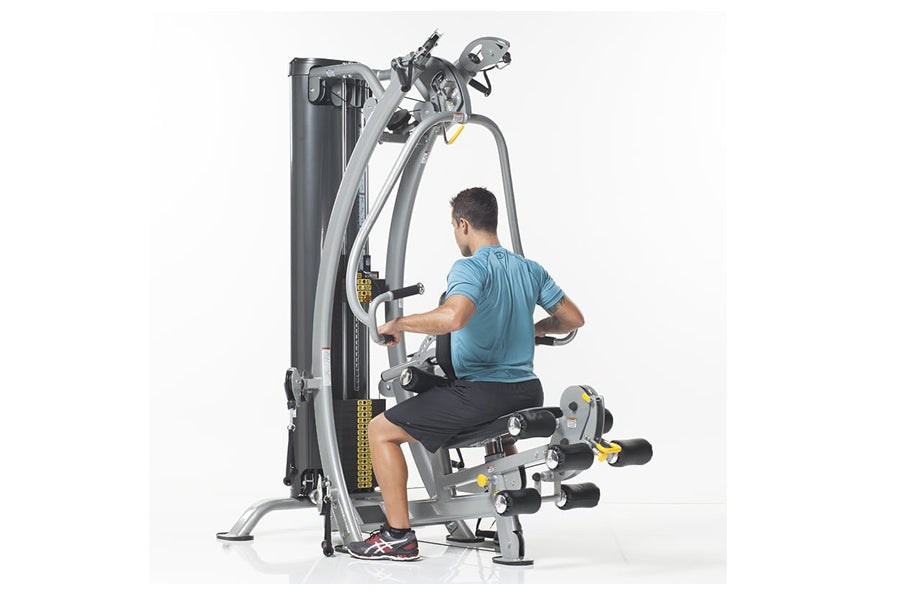 Man in blue shirt using gray and black multi-station home gym machine with leg press attachment on white background