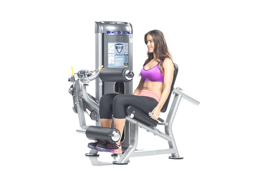 Woman in purple sports bra and black leggings using silver and black leg extension machine with digital display on white back