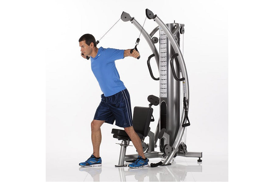 Man in blue shirt using silver and black functional trainer machine with cable handles on white background