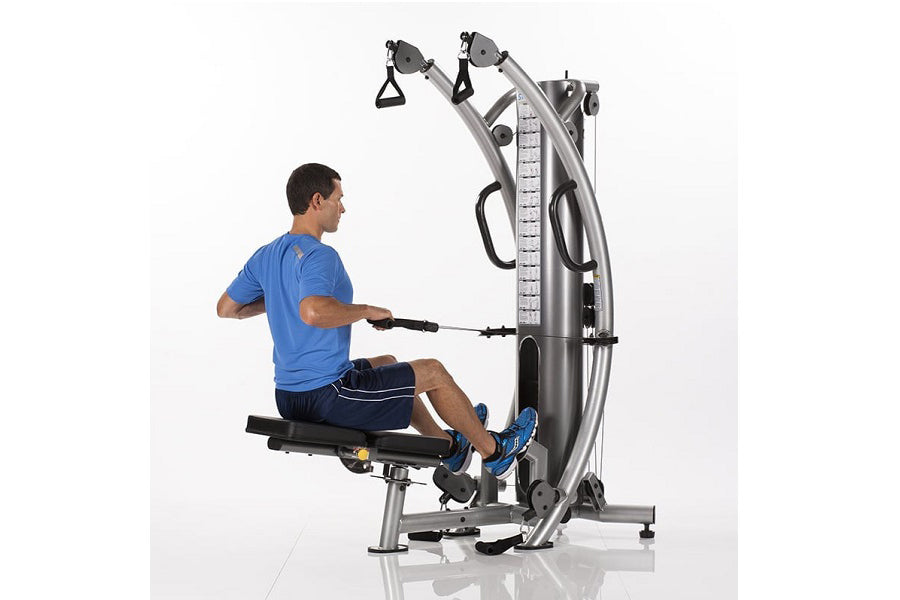 Man in blue shirt using silver and black functional trainer machine with dual cable system on white background