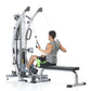 Male user demonstrating silver and black cable machine trainer with dual pulleys and height measurement scale, seated on blac