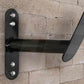 Black metal wall-mounted rope hanger with adjustable arm and chrome bolts, mounted on brick wall
