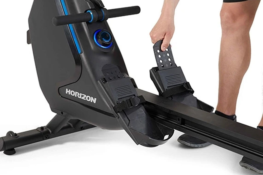 Horizon Oxford 6 black rower with blue accents, shown with model's foot on footrest and hand on console