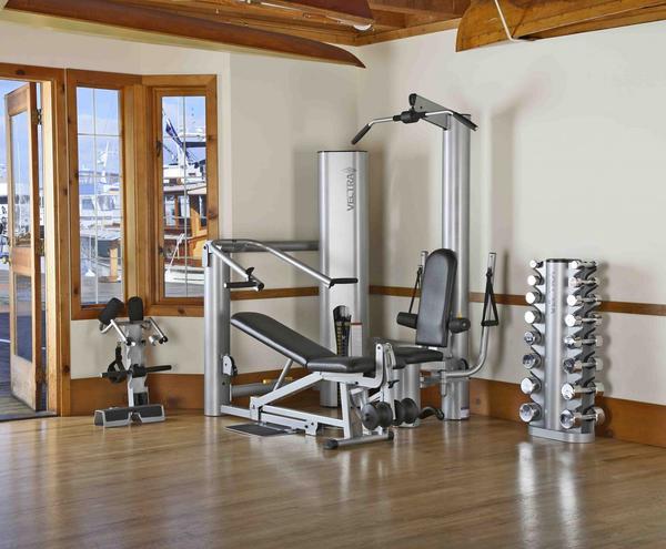 Silver and black multi-station home gym with leg press, chest press, and weight stack on wooden floor in gym room