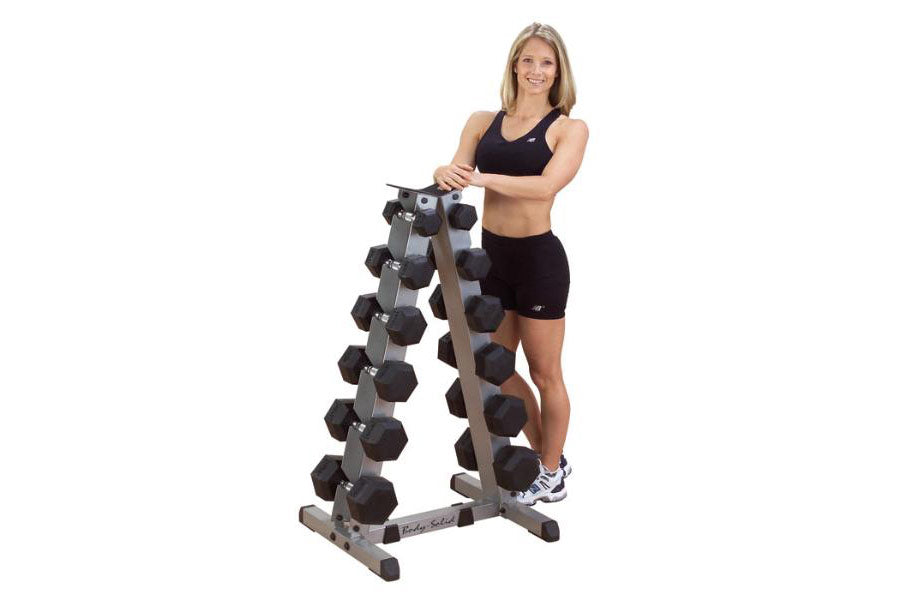 Woman wearing black sports bra and shorts standing next to vertical A-frame dumbbell rack with multiple pairs of hexagonal bl