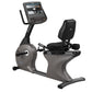 Gray and black recumbent exercise bike with digital display screen, black padded seat, and foot pedals on white background