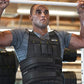 Man wearing SKLZ black weighted vest with gray athletic shirt, performing pull-up exercise in gym