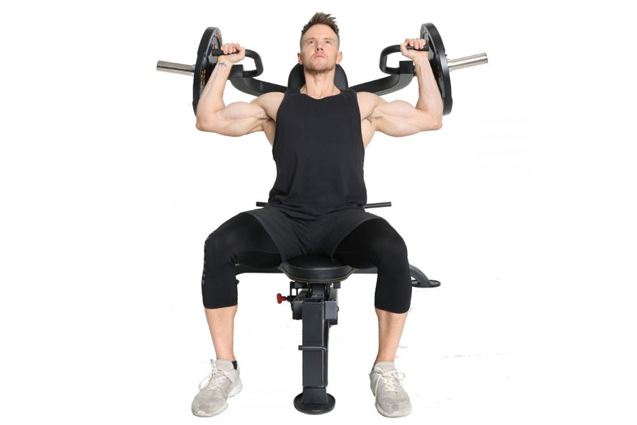 Male athlete seated on black weight bench performing dumbbell shoulder press with weighted barbells, wearing black sleeveless