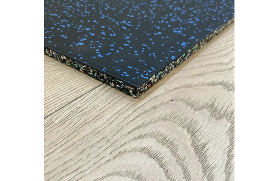 Black and blue speckled rubber gym tile with gold-trimmed edge on light wood grain textured floor