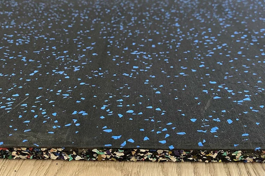Black rubber gym flooring tile with blue fleck pattern and colorful speckled border, shown on wood floor