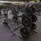 Busy gym floor with stationary bikes, weight plates, and dumbbells on gray interlocking rubber tiles