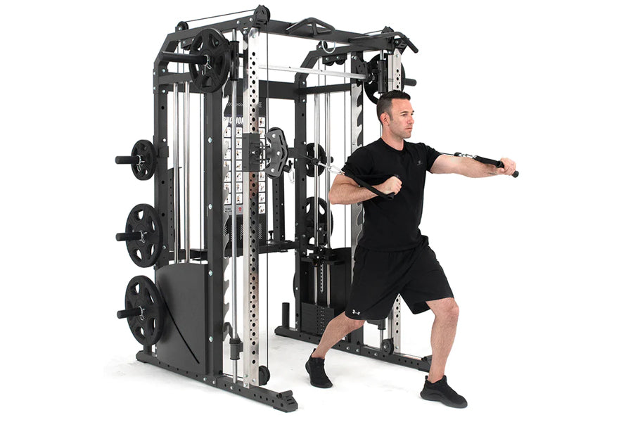 Man in black shirt and shorts demonstrating Warrior 701 black and white multi-station power rack with cable crossover and smi