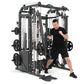 Man in black shirt and shorts using black and white multi-station home gym with cable crossovers and smith machine on white b