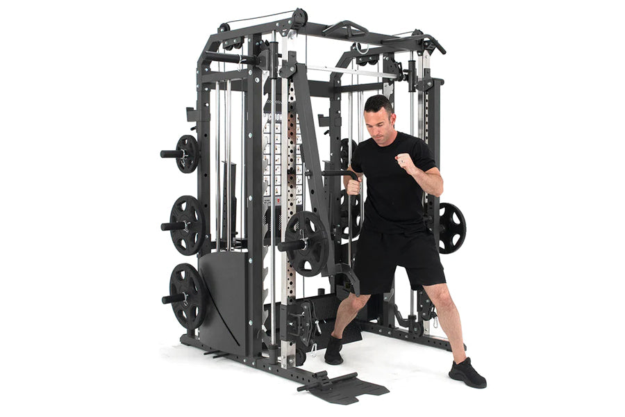 Man in black shirt and shorts using black and white multi-station home gym with cable crossovers and smith machine on white b