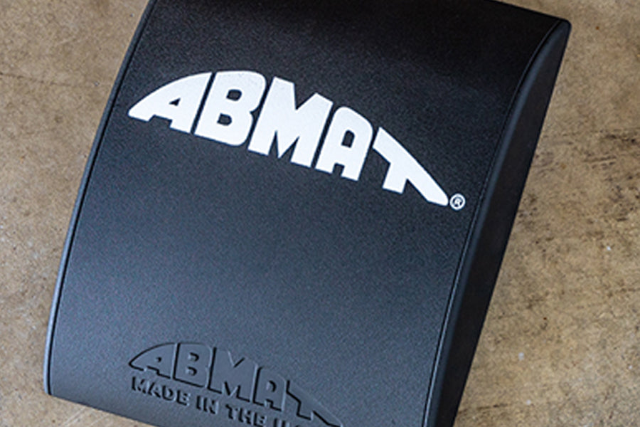 Navy blue AbMat core training pad with white ABMAT logo and curved design, flat lay on concrete background