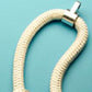 Cream-colored textured rope bracelet with silver toggle clasp on turquoise background