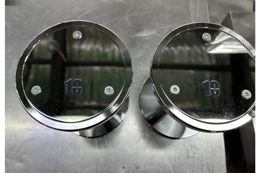 Pair of chrome dumbbell end caps with "18" markings and adjustment holes, displayed on gray surface