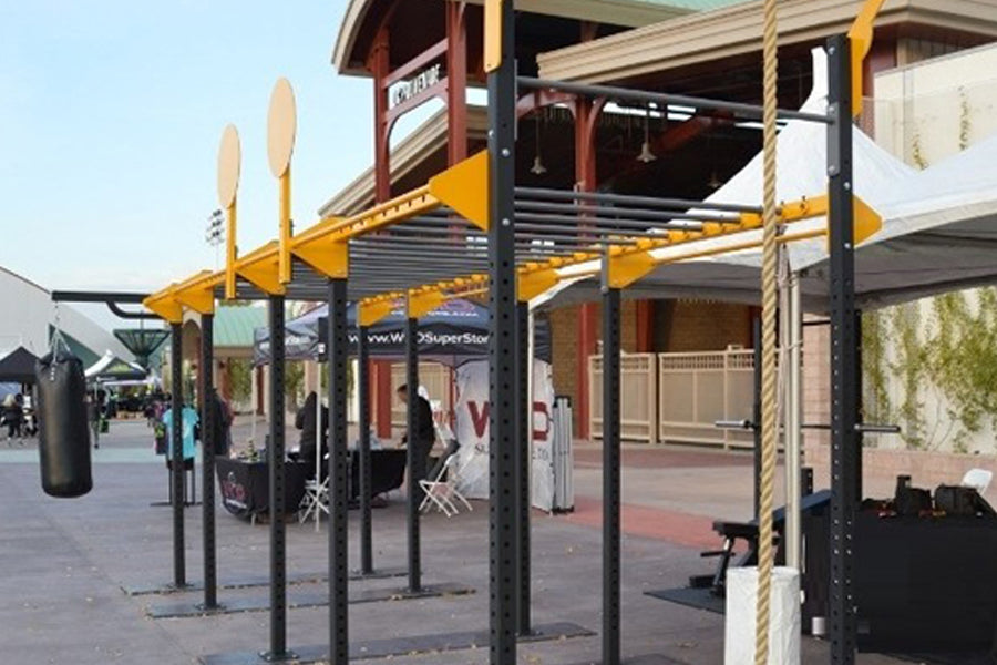 Yellow and black metal outdoor fitness rig with pull-up bars, rope climbs, and mounted equipment in commercial setting