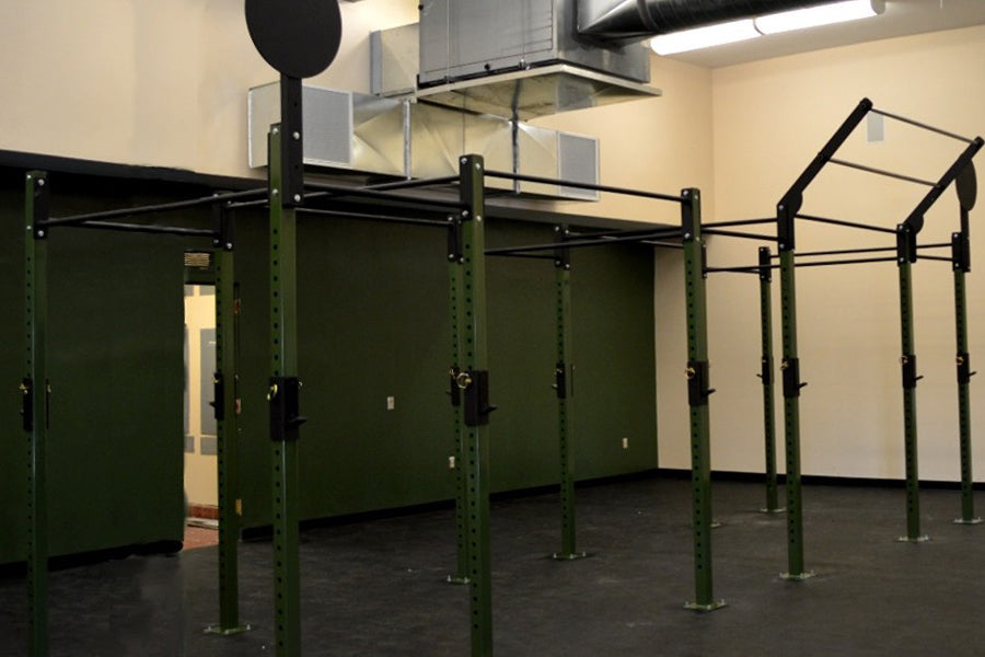 Warrior Commercial Pro Rig System with olive green steel frame, black pull-up bars, and perforated uprights in gym setting