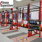 Commercial gym rig system with red and black steel frames, pull-up bars, weight plates, and resistance bands in fitness facil