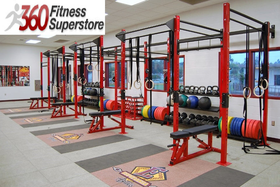 Commercial gym rig system with red and black steel frames, pull-up bars, weight plates, and resistance bands in fitness facil