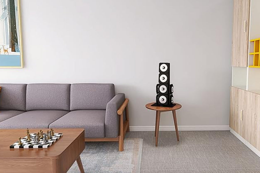 Black four-speaker stacked tower with white cone drivers on wood side table in modern living room setting