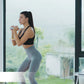 Black sports bra and gray leggings worn by model holding adjustable dumbbell during workout by window