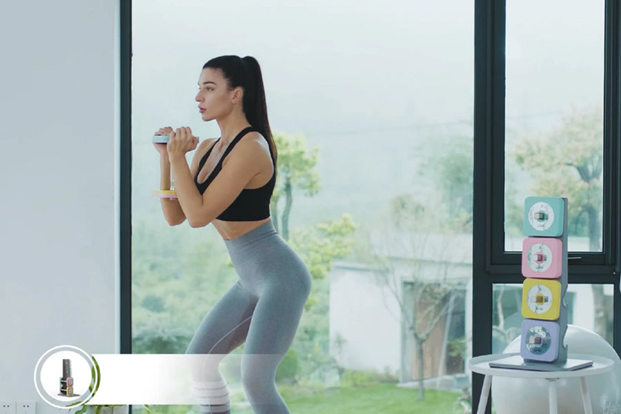 Black sports bra and gray leggings worn by model holding adjustable dumbbell during workout by window