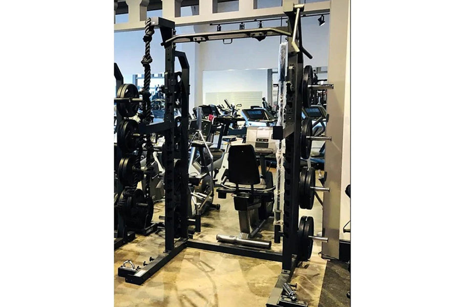 Black power squat rack with adjustable safety bars and weight plate storage, shown in gym setting