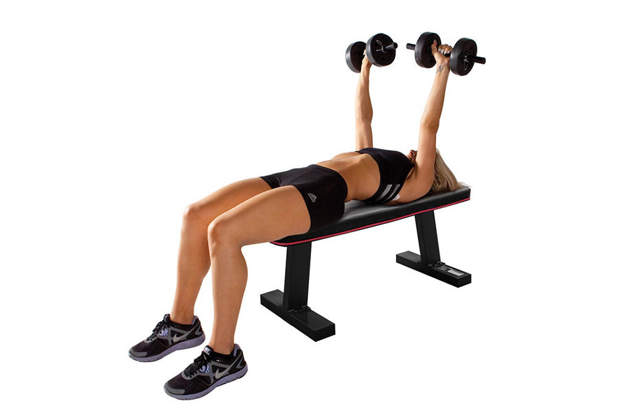 Woman performing dumbbell chest press on black flat weight bench with red trim