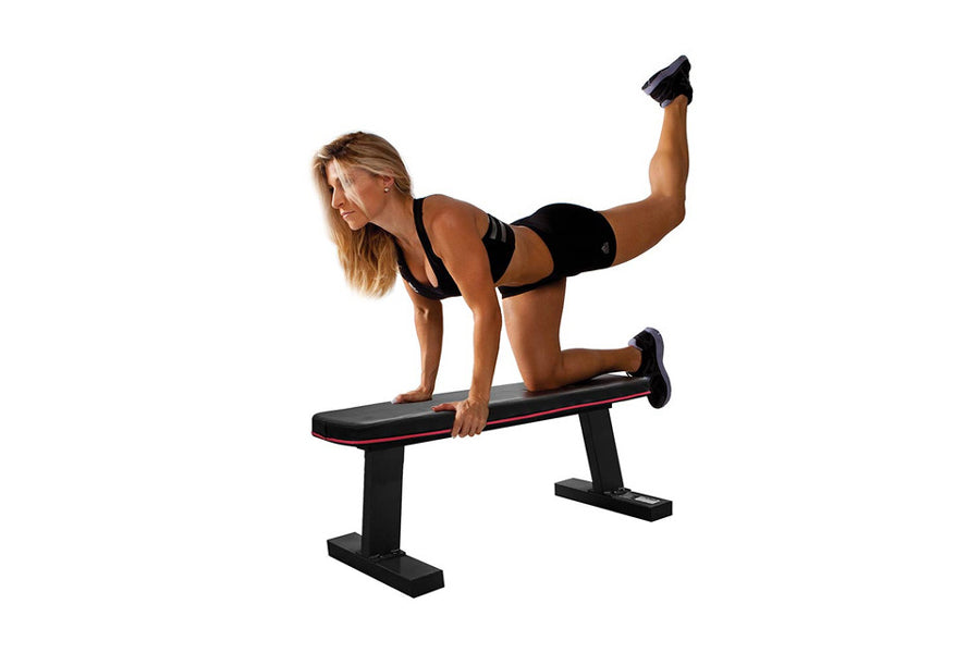 Woman performing leg lift exercise on black flat weight bench with red trim against white background