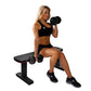 Woman in black sports bra and shorts sitting on black flat weight bench, holding dumbbell in bicep curl position, white backg