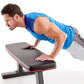 Man in blue tank top performing push-up exercise on black and red flat weight bench against white background