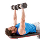 Man in blue tank top lying on black and red weight bench performing dumbbell press with gray hexagonal dumbbells