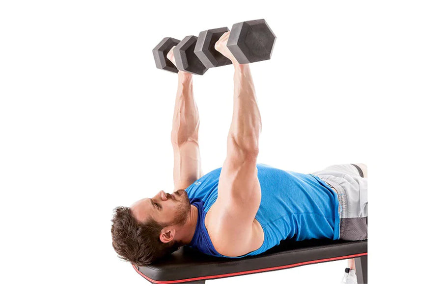 Man in blue tank top lying on black and red weight bench performing dumbbell press with gray hexagonal dumbbells