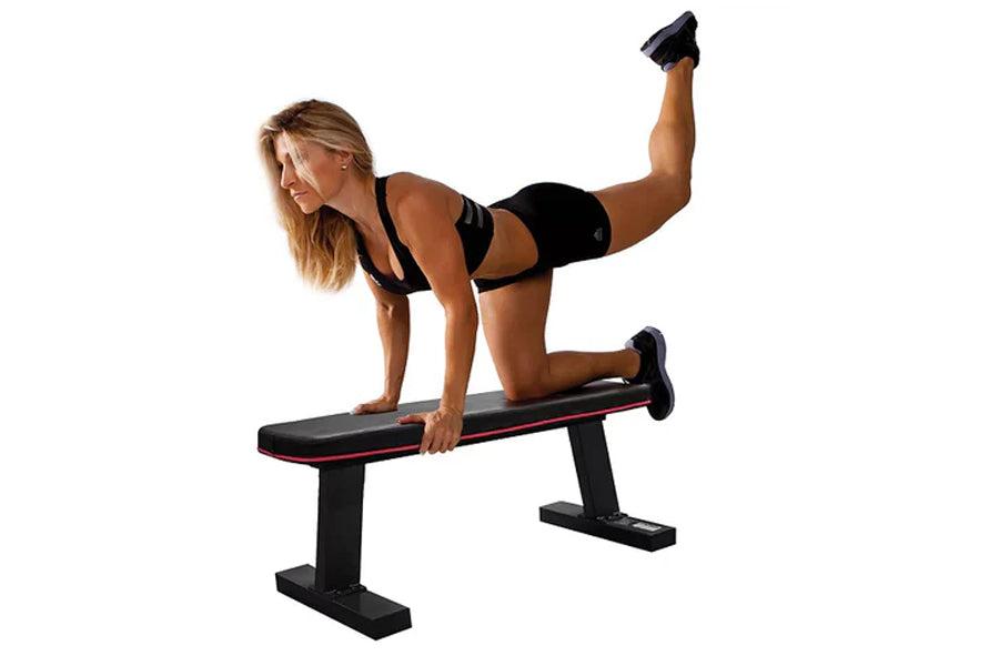 Woman performing leg lift exercise on black and red flat weight bench with dumbbells