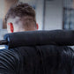 Person wearing black t-shirt holding barbell with black foam shoulder pad for squats in gym setting